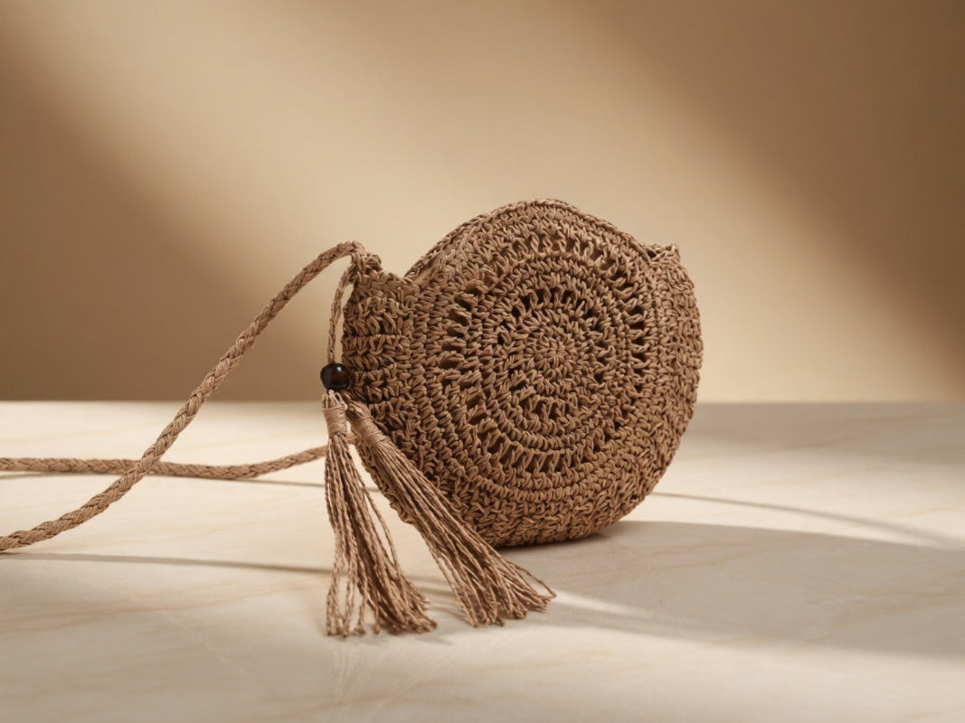 Round woven bag with tassel on a light wooden surface